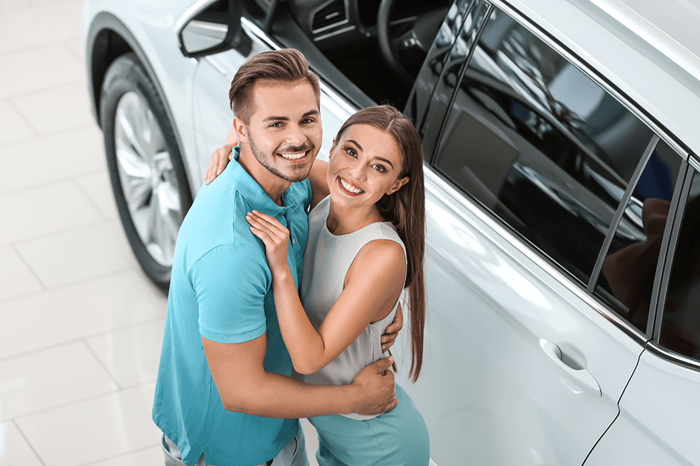 happy-couple-embracing-by-new-car-in-showroom-2026-03-05-11-41-20-utc.png